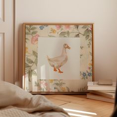 a white duck sitting on top of a wooden floor next to a framed photo with flowers