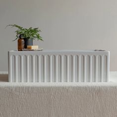 a white radiator sitting on top of a bed next to a potted plant