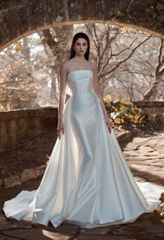 a woman in a white wedding dress posing for the camera with trees and rocks behind her