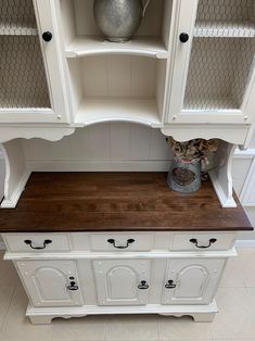 a white hutch with wood top and drawers on the side, next to a vase