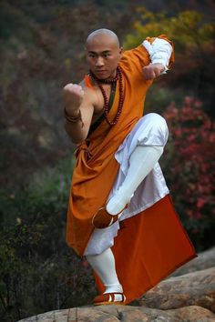 a man in an orange and white outfit standing on rocks with his arms out to the side