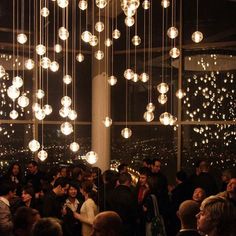 a large group of people standing in front of a window with lights hanging from the ceiling