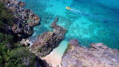 a boat is in the water near some rocks and blue water with green trees on either side