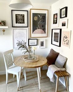 a small table with some flowers on it in front of pictures and framed art hanging on the wall