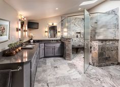 a large bathroom with marble counter tops and gray cabinets, along with a walk in shower