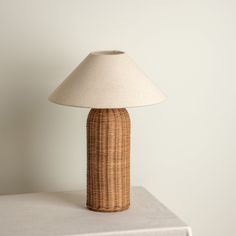 a wicker lamp sitting on top of a table next to a white cloth covered wall