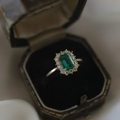 an emerald and diamond ring in a black box