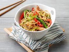 a white bowl filled with noodles and vegetables on top of a wooden cutting board next to chopsticks