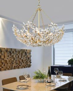 a chandelier hanging over a dining room table with place settings on the side