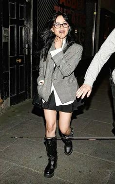 a woman walking down the street with her hand in her mouth while wearing black boots