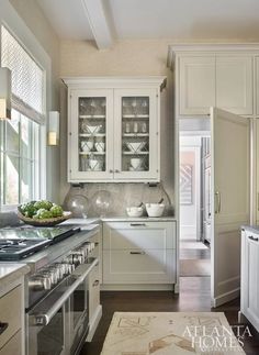 a kitchen with lots of white cabinets and glass doors on the front door, along with an area rug that matches the hardwood floor