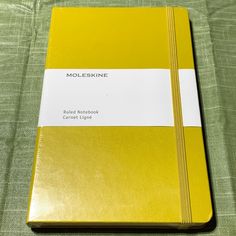 a yellow and white notebook sitting on top of a green cloth covered tablecloth with the words molleskinne