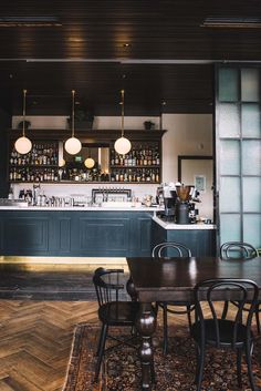 an empty restaurant with wooden floors and dark green cabinets, along with black dining chairs