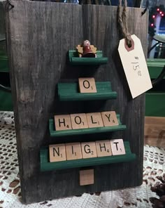 a christmas tree made out of scrabble tiles on a wooden board with a tag hanging from it