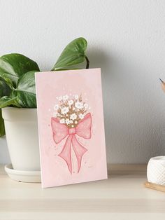 a pink greeting card with a bow and flowers on it art boarder next to a potted plant