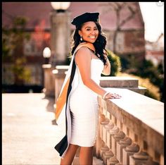 a woman in a graduation cap and gown leaning on a wall