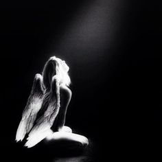 a black and white photo of an angel sitting on the ground with its wings spread