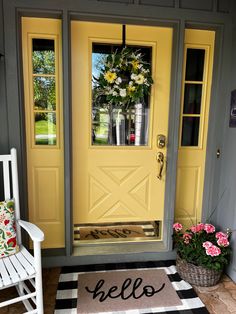 a yellow door with the word hello written on it next to a white rocking chair