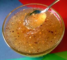 a spoon is in a glass bowl filled with some kind of sauce on a colorful table cloth