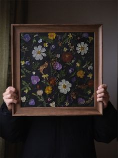 a person holding up a framed painting with flowers on it's back and arms