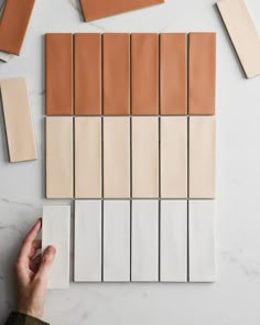 a person holding a piece of paper next to some tiles on a table with different colors