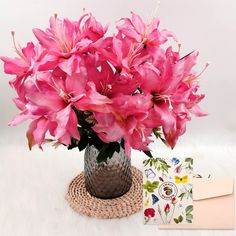 a vase filled with pink flowers next to a card and envelope on a white surface