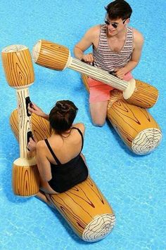 two people sitting on top of wooden rafts in an indoor swimming pool with blue water