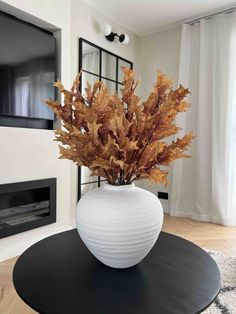 a white vase filled with lots of brown leaves sitting on top of a black table