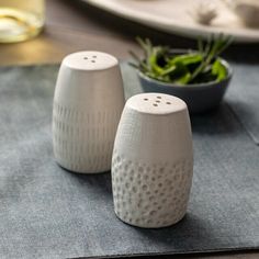 two salt and pepper shakers sitting on top of a table next to a plant