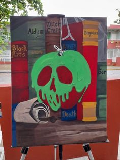 an easel with a painting of a green skull on it's face and books in the background