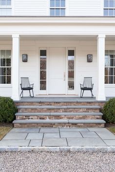 two chairs sitting on the front steps of a white house with columns and windows,