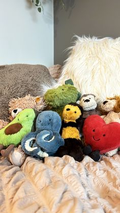 a pile of stuffed animals sitting on top of a bed next to a white pillow