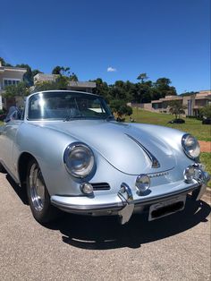 an old silver sports car parked on the side of the road in front of a house