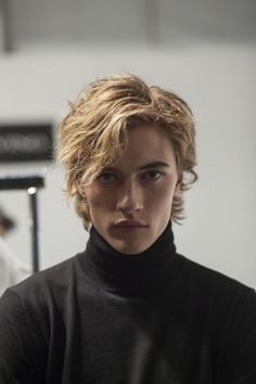 a woman with short blonde hair wearing a black turtle neck sweater and looking at the camera