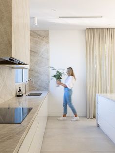 a woman standing in a kitchen next to a sink and counter top with a potted plant on it