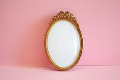 an oval shaped mirror on a pink wall with gold trimmings and ornate detailing