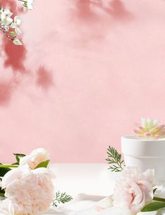 a table topped with a white cake covered in flowers and greenery next to a pink wall