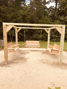 a wooden swing set in the middle of a sandy area with trees in the background