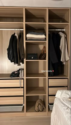 an open closet with clothes and shoes on shelves in front of a white bed sheet