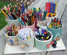 several cups filled with pencils and markers on a picnic table