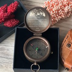 an antique pocket watch sits in a box next to some flowers and a leather wallet