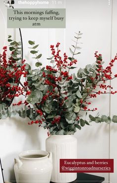 a white vase filled with red berries and greenery