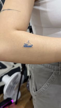 a woman's arm with a small boat tattoo on the left side of her arm