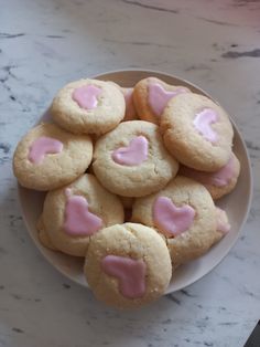 a white plate topped with cookies covered in pink frosted heart shaped icing on top of a marble counter