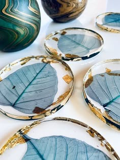 four plates with blue leaves on them sitting on a table next to two vases