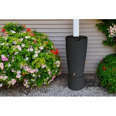 a tall black vase sitting next to some bushes and flowers in front of a house