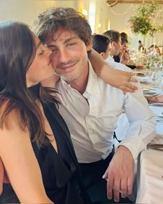 a man and woman kissing each other at a dinner table with people in the background