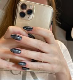 a woman holding up her cell phone with black and silver nail polishes on it