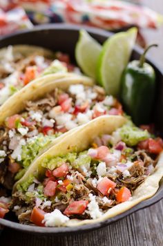 three tacos in a cast iron skillet with lime wedges on the side