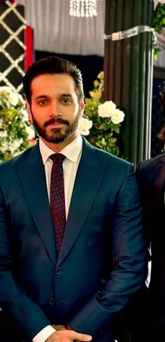 two men in suits and ties standing next to each other with flowers on the wall behind them